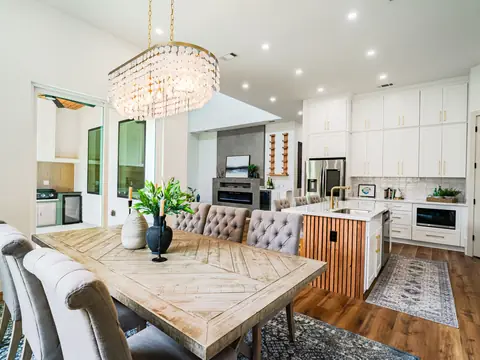 A bright kitchen with white cabinets, a long island and a wooden dining table