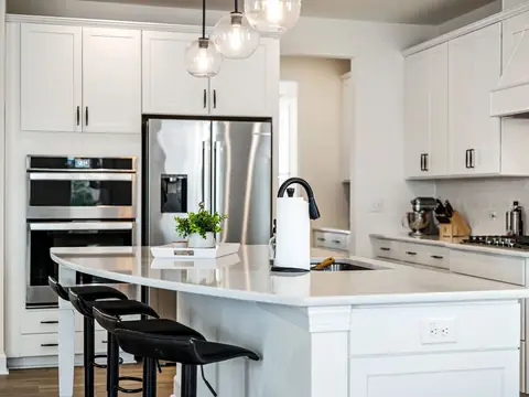 A white stone island with a black faucet, black stools and white cabinets behind