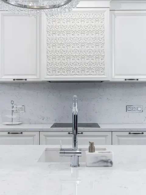 A chrome faucet over a polished white veined stone countertop