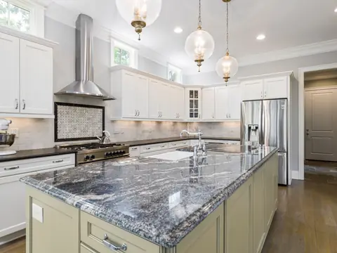 A kitchen island with a dark veined granite top under glass pendant lights