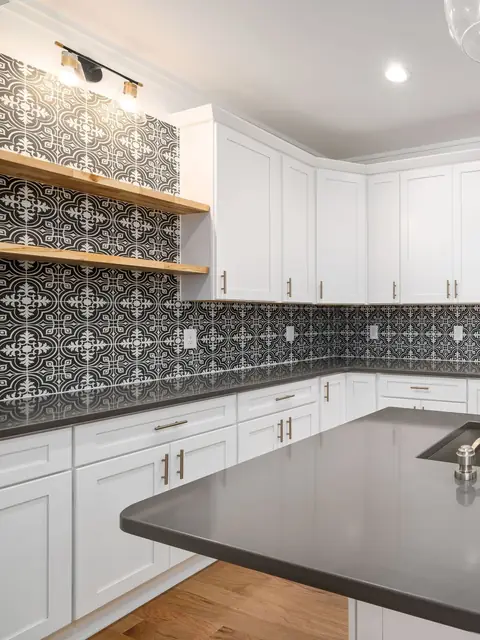 Black and white patterned wall tile above white shaker cabinets and a grey counter