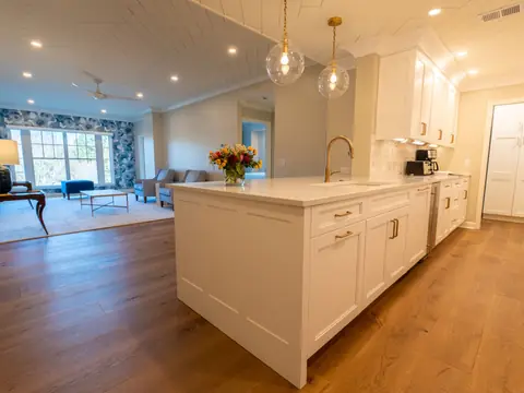 A white kitchen island with a sink and pendant lights in a bright open room