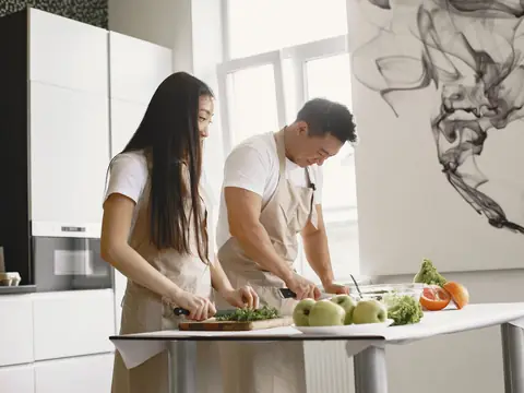 Two people cutting vegetables at a simple white table in a bright room