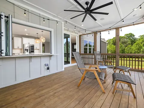 A screened porch with a pass-through window to a white kitchen and wooden chairs