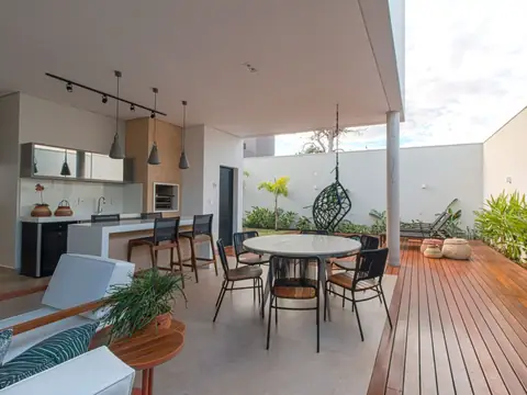 A covered patio kitchen with a counter, a round table and a wooden deck in sunshine
