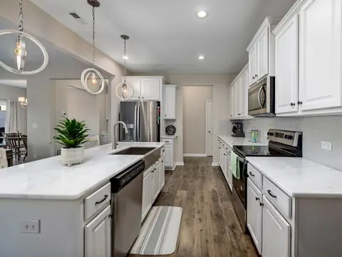 A bright galley kitchen with white cabinets, marble counters and ring pendant lights